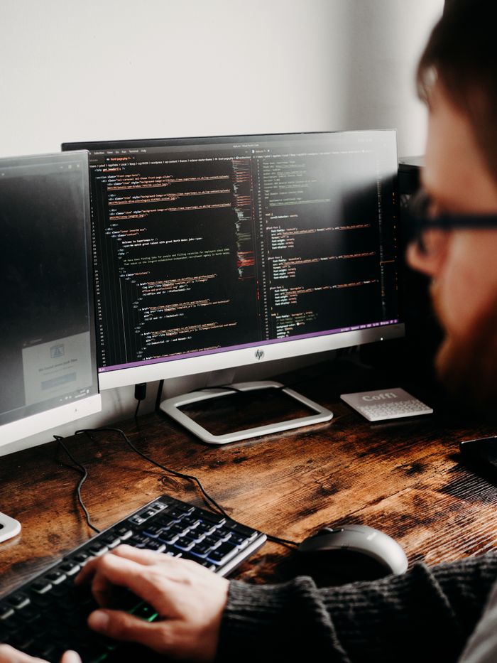 our-story Focused software developer at desk coding with multiple monitors in a modern workspace.