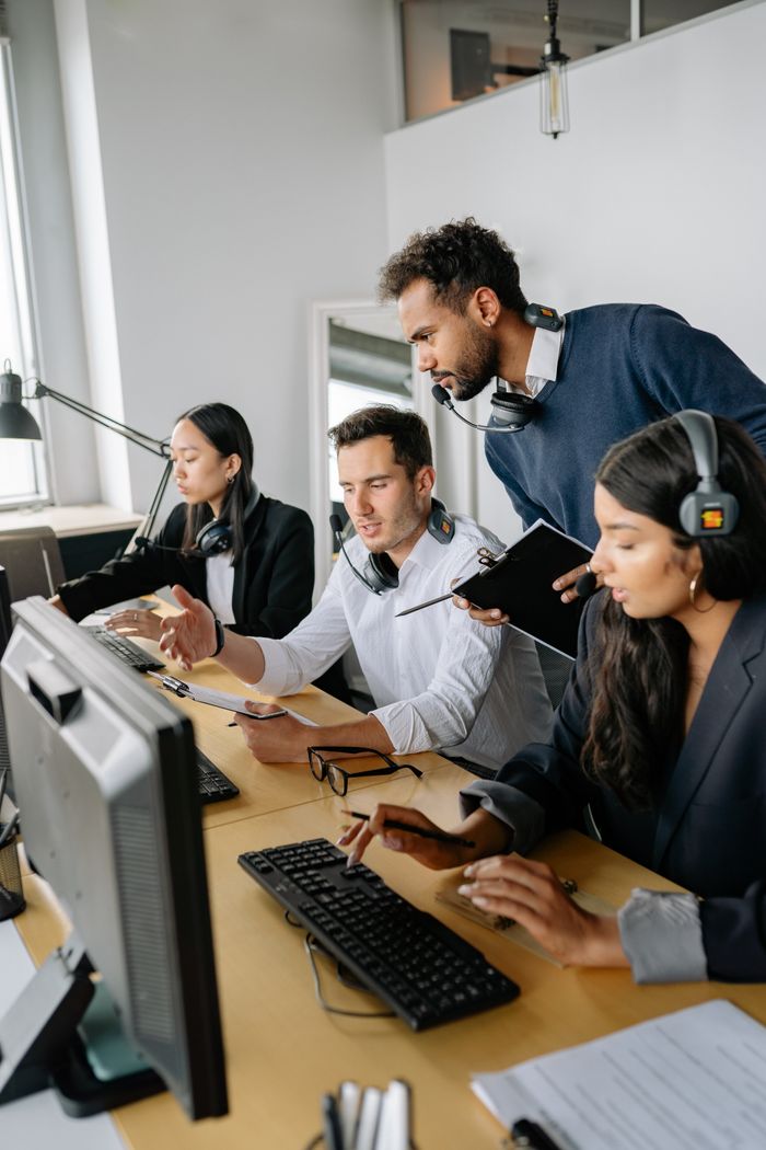 A diverse group of call center employees working and collaborating at desks with headsets in a modern office.